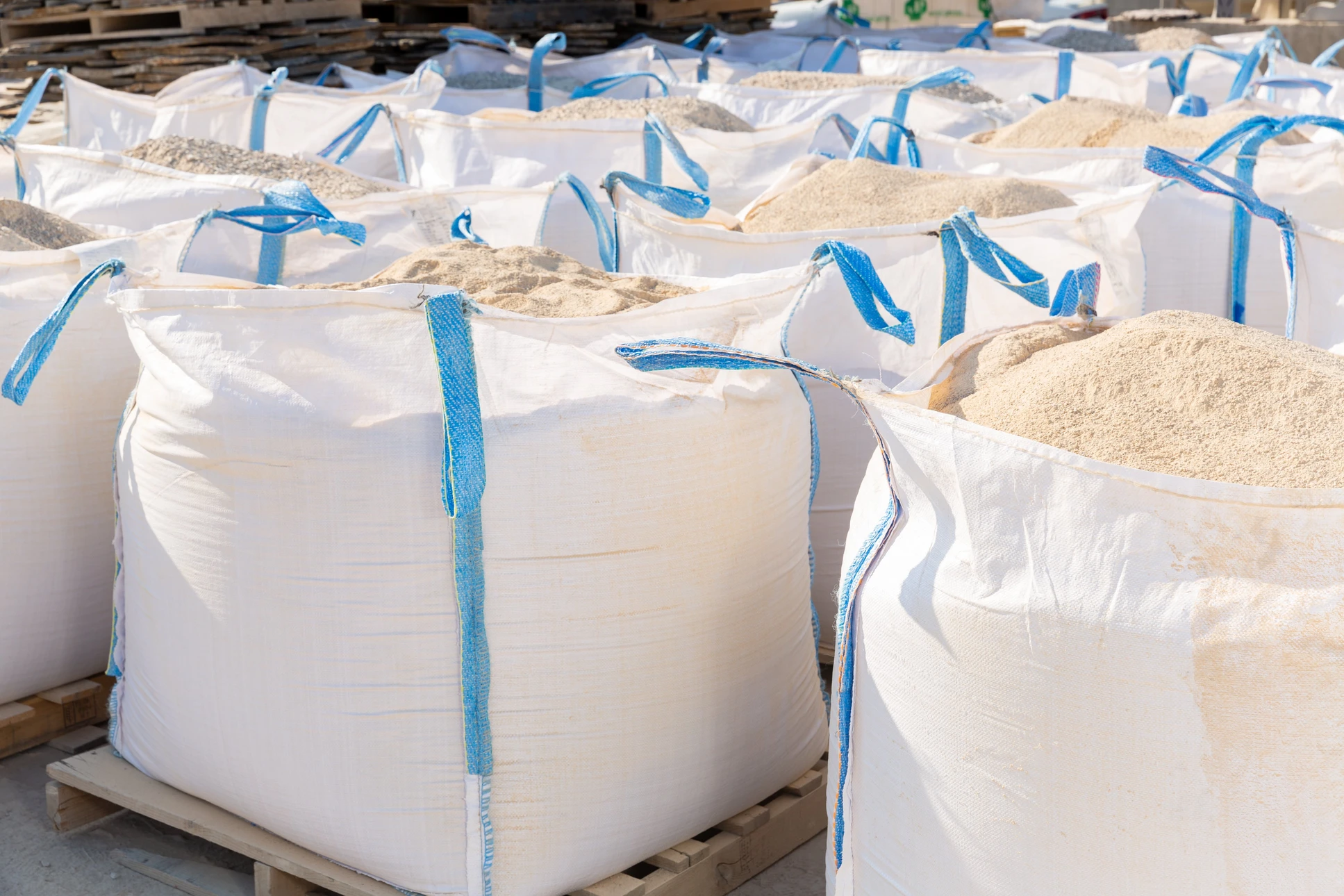 Espace de stockage extérieur avec nombreux big bags blancs aux sangles bleues disposés sur palettes en bois